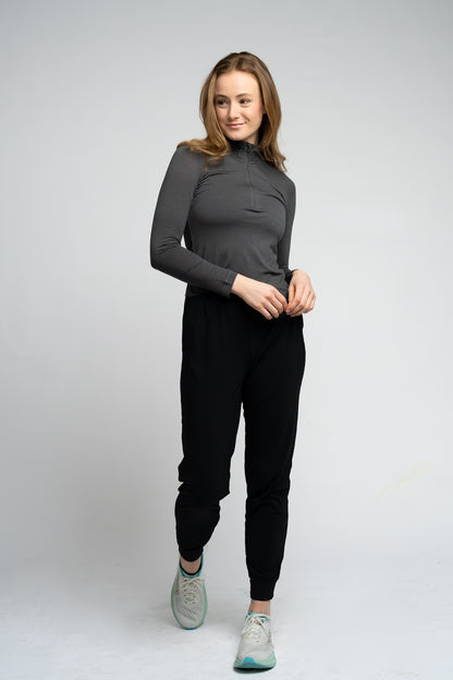 Woman wearing a dark gray long-sleeve top and black jogger pants on a white background