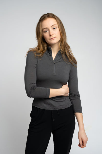 Woman wearing a gray long-sleeve top and black pants on a light gray background