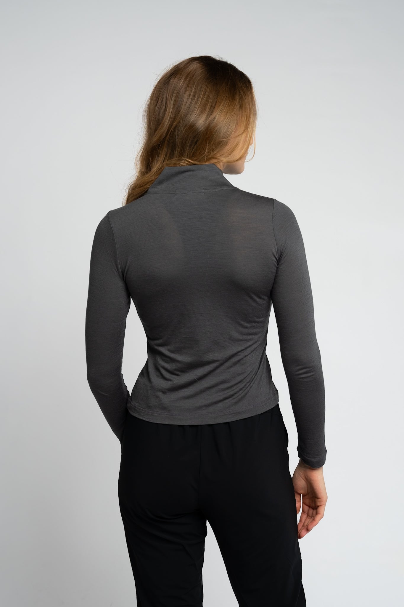 Person wearing a gray long-sleeve top and black pants on a light gray background