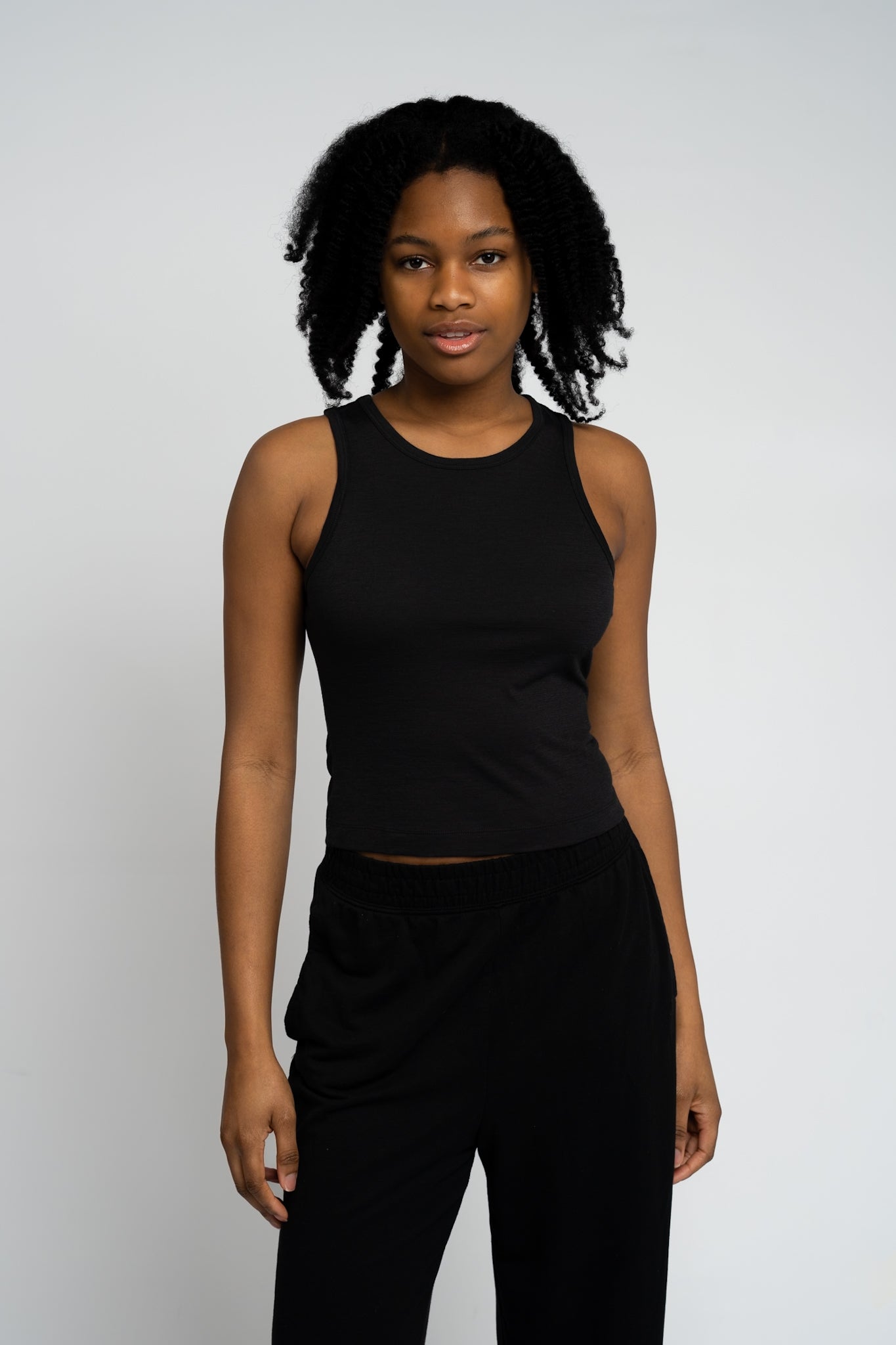 Woman wearing a black sleeveless top and black pants against a white background