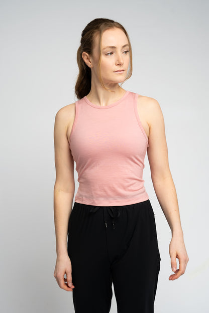 Woman wearing a pink sleeveless top and black pants on a light gray background