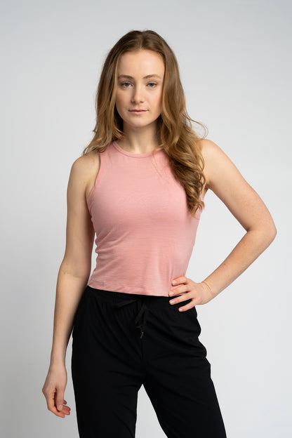 Woman wearing a pink sleeveless top and black pants on a light gray background