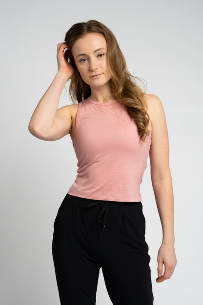 Woman wearing a pink sleeveless top and black pants against a plain background