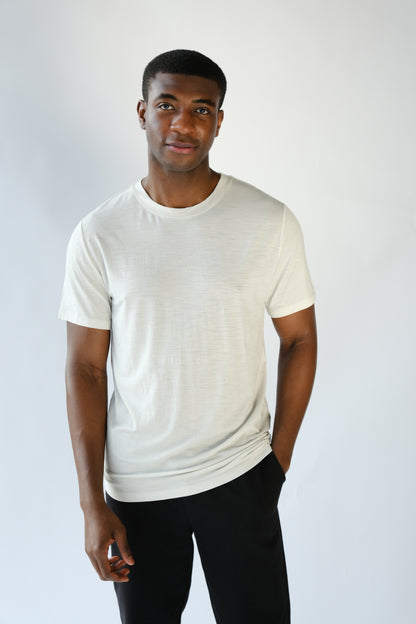 Man wearing a plain white t-shirt and black pants against a light gray background