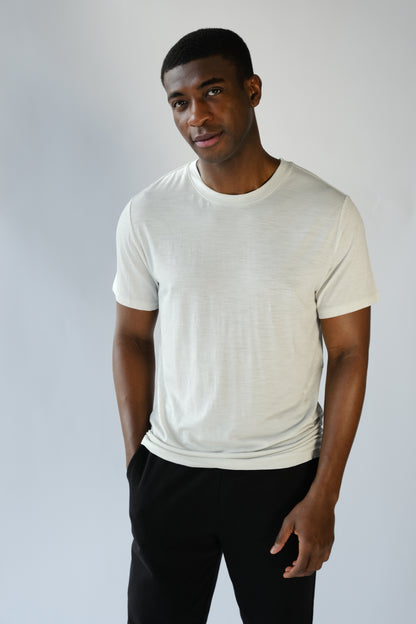 Man wearing a plain white t-shirt and black pants against a light gray background