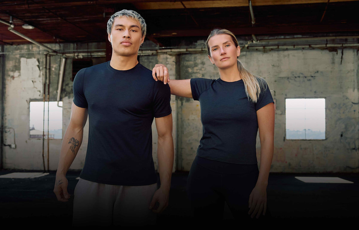Two models wearing matching dark navy athletic t-shirts in an industrial warehouse setting.